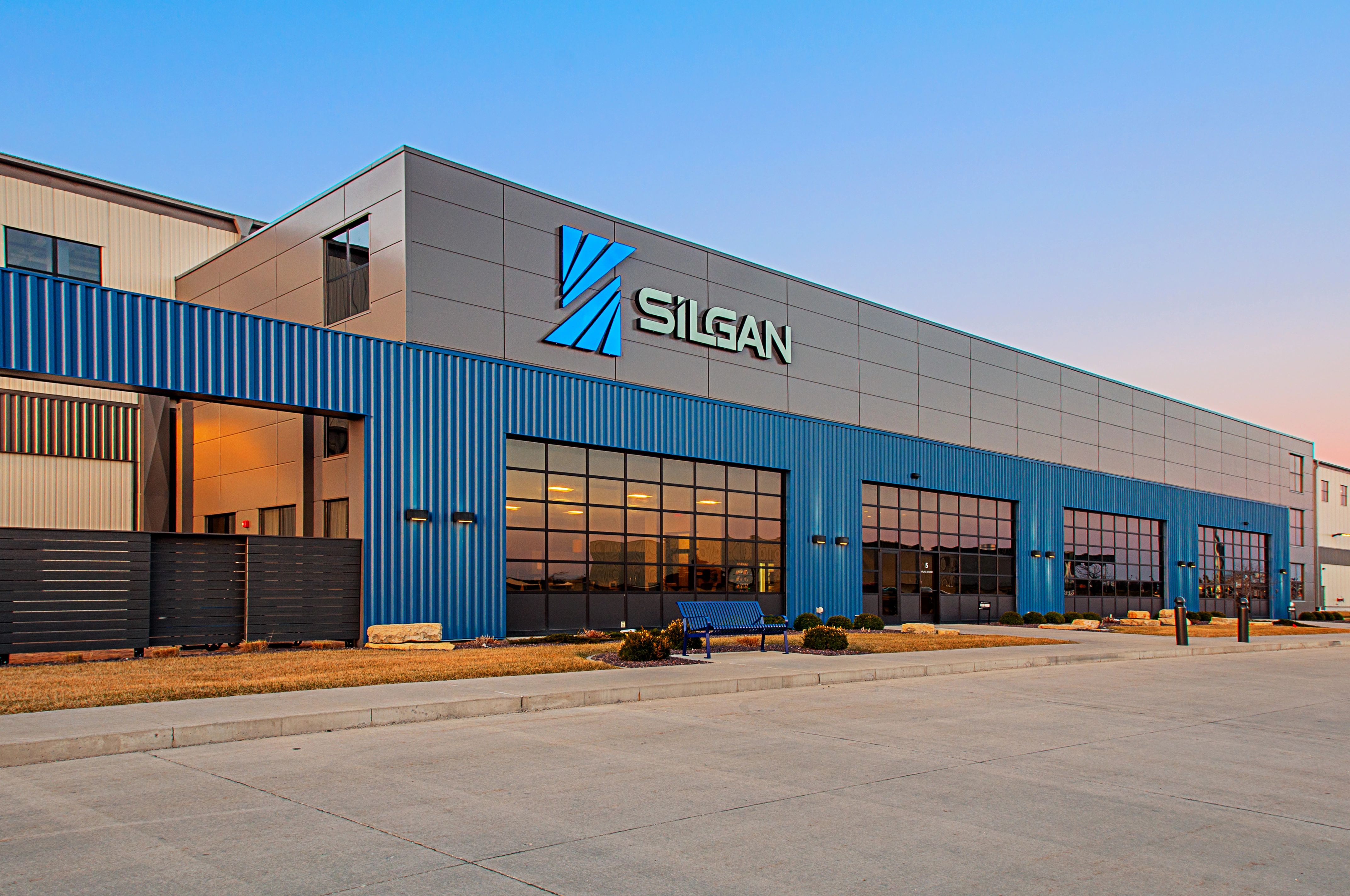 An unoccupied blue bench is seen in front of a building labelled Silgan